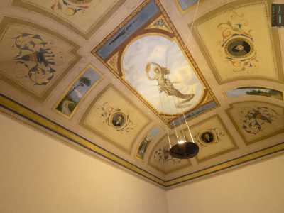 La parte centrale, delimitata da una cornice dorata intrecciata, mostra una scena celestiale con una sinuosa figura femminile centrale ispirata alle Muse